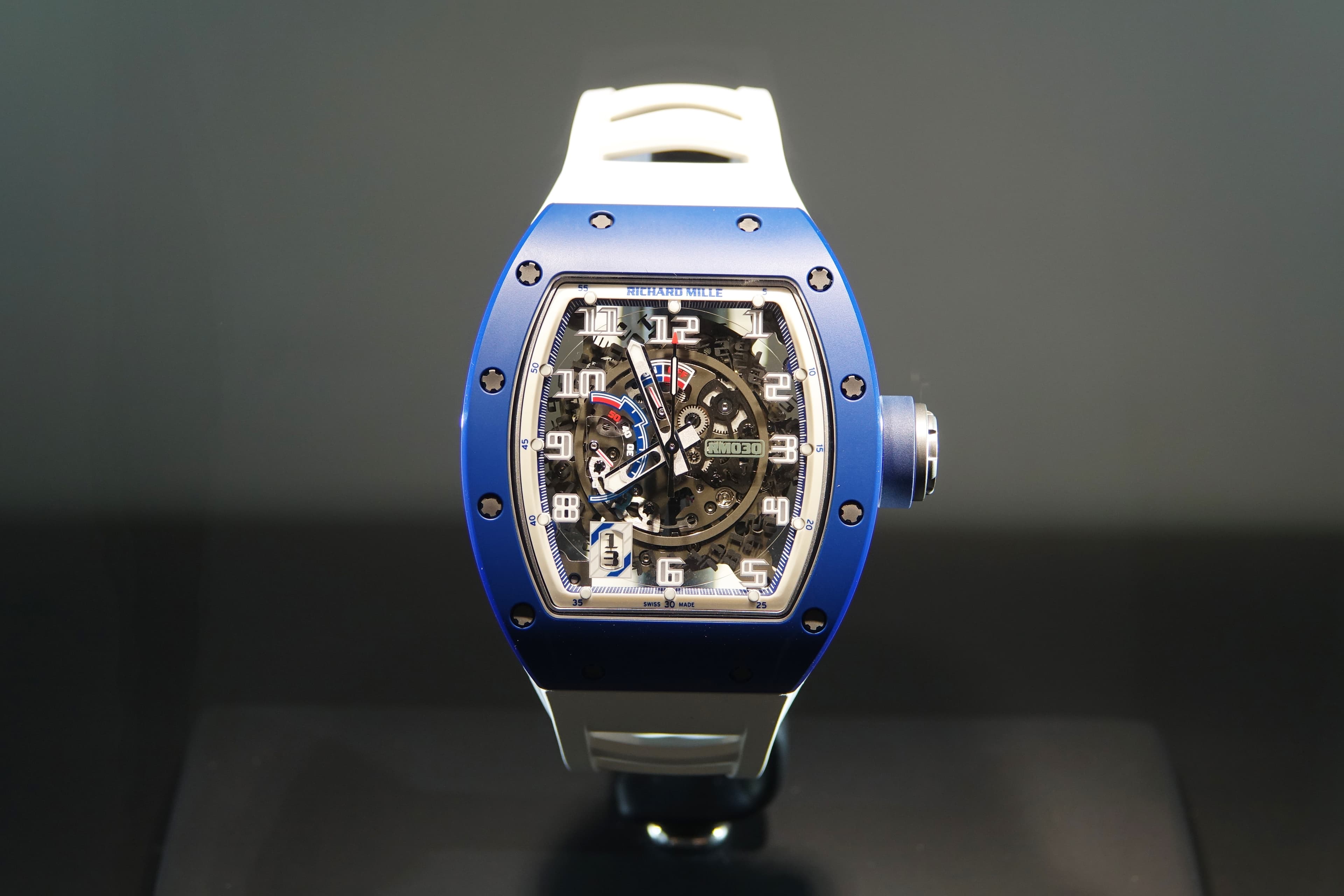 Luxury Richard Mille watch with a blue tonneau case, skeletonized dial, and white rubber strap.